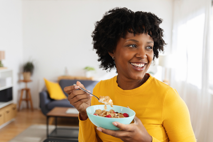 Smiling woman enjoying healthy breakfast of whole grain cereal with raspberries